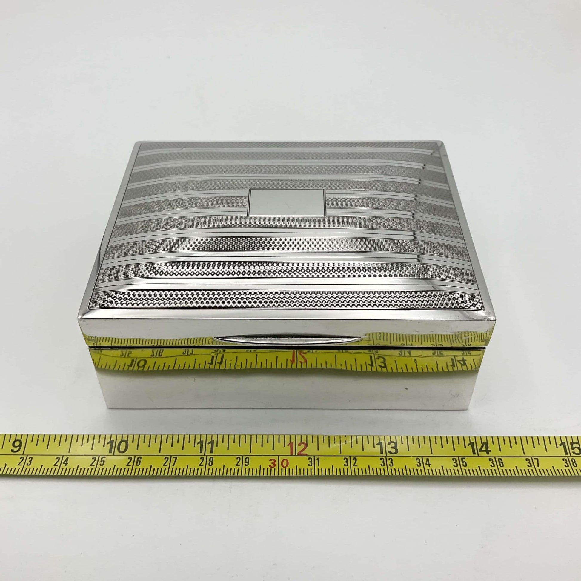 1920s vintage silver cigarette box next to a tape measure showing it's width as 10.5cm