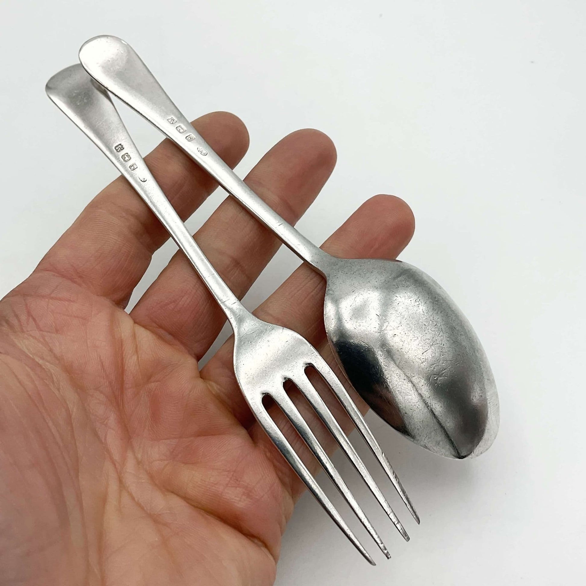A matching silver spoon and fork sitting on a hand showing the back view.