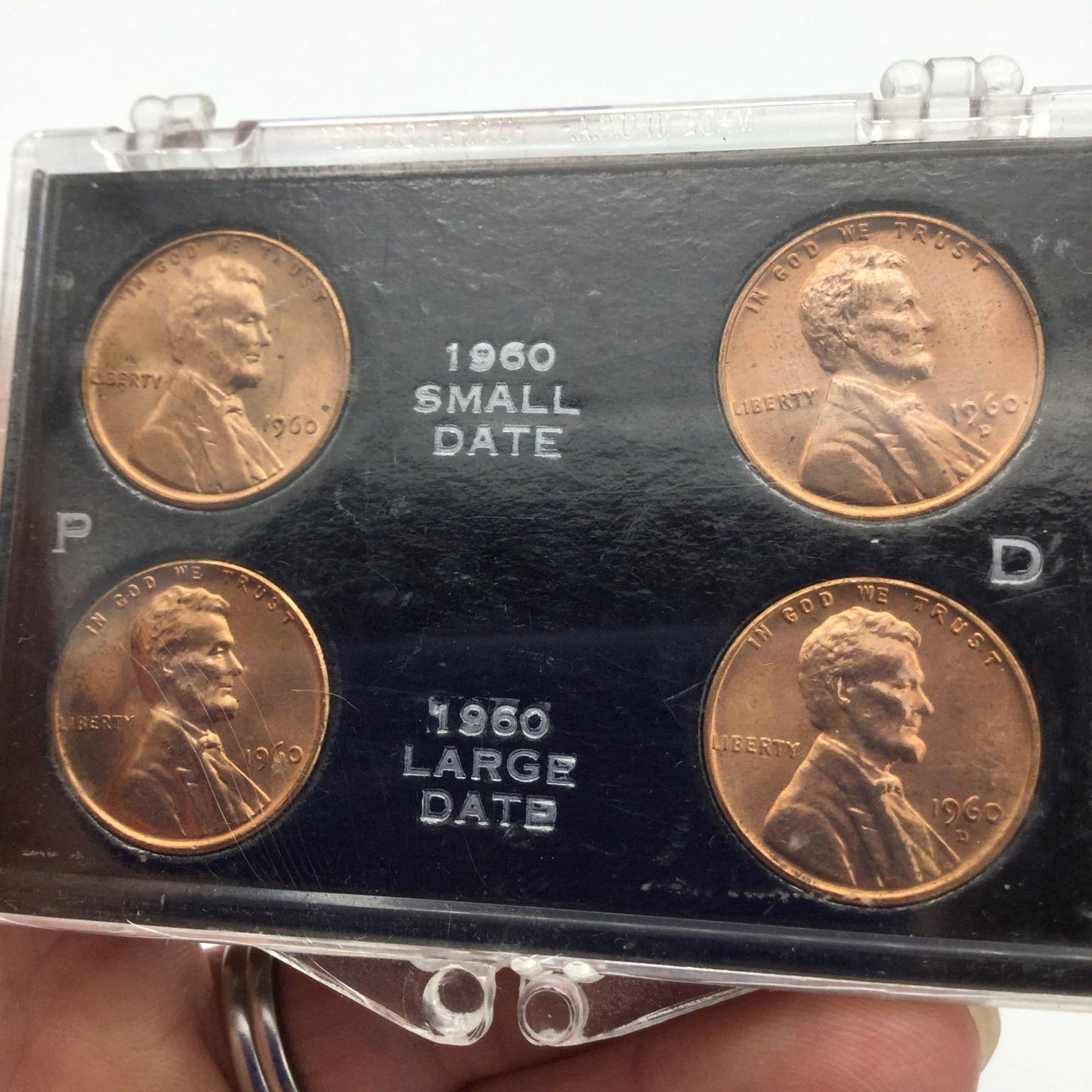 Four Lincoln Memorial Cents in a black holder and perspex case. It has P and D on the blakc holder and 1960 small date and 1960 large date on the black holder held in a hand