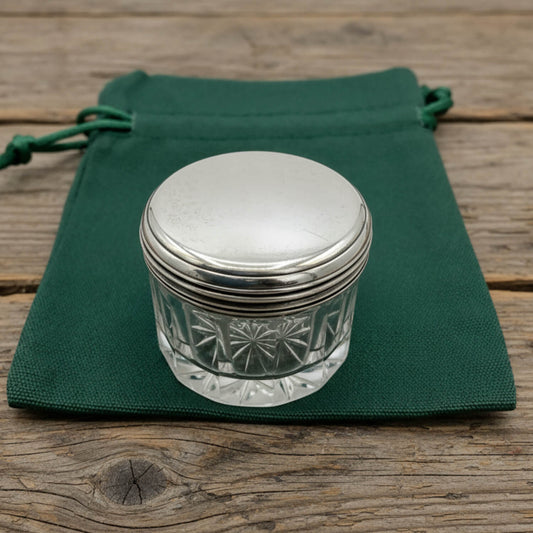 Silver-lidded glass jar on a green cloth with a wooden background