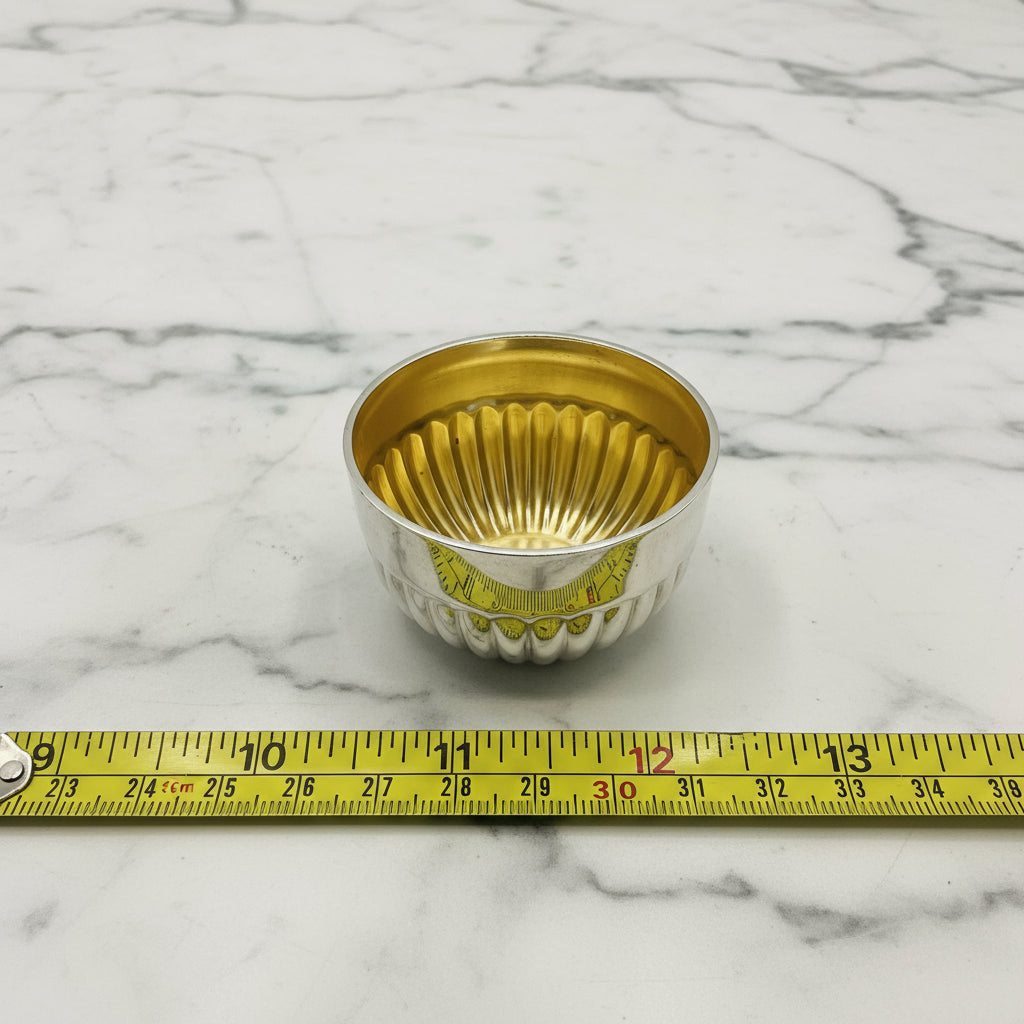 Glided silver Victorian salt next to a tape measure showing the diameter as 2.5cm on a white background