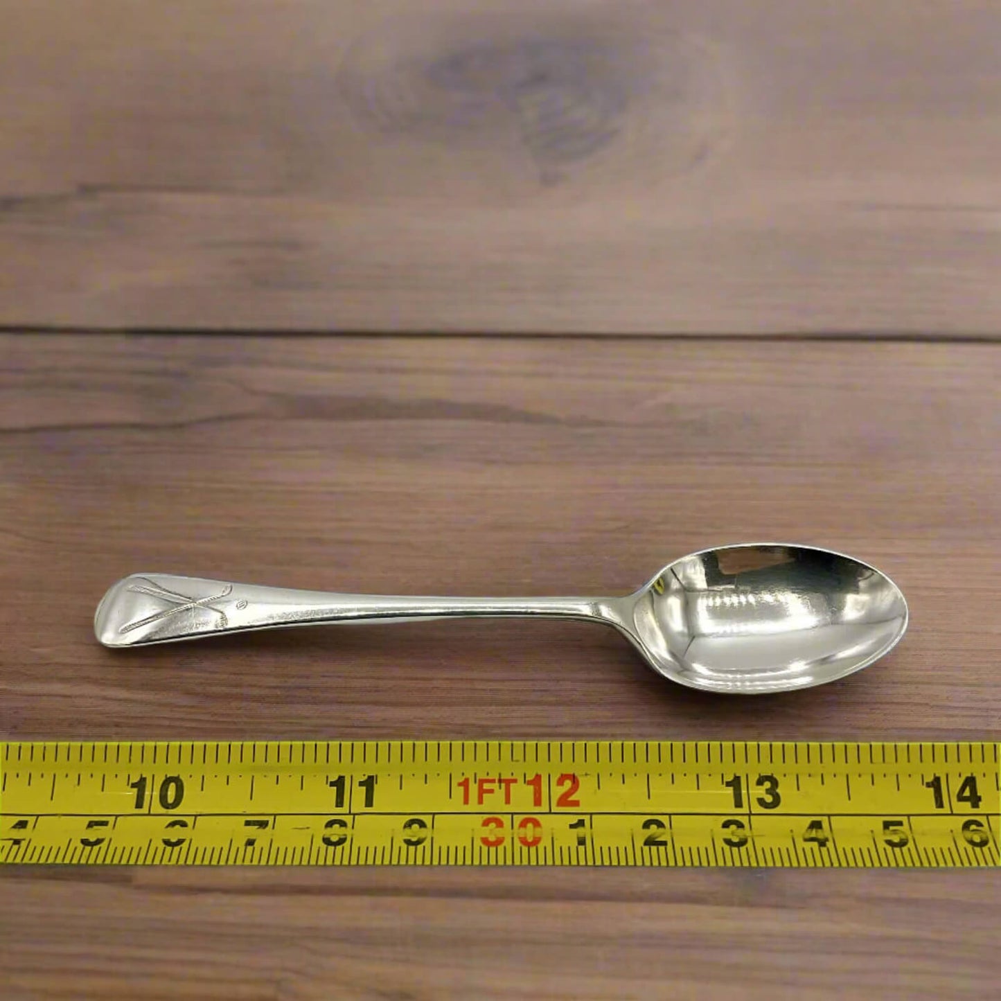Silver spoon on a wooden surface with a yellow measuring tape for scale.