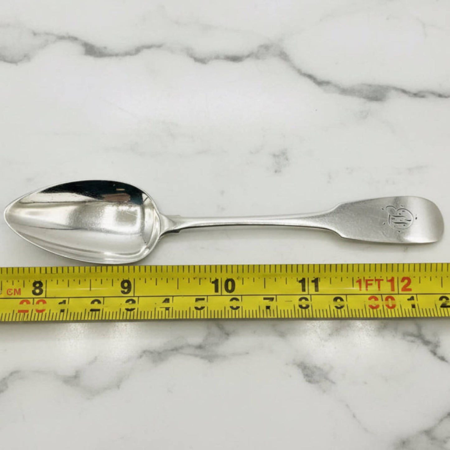 Silver spoon on a marble surface with a measuring tape for scale.