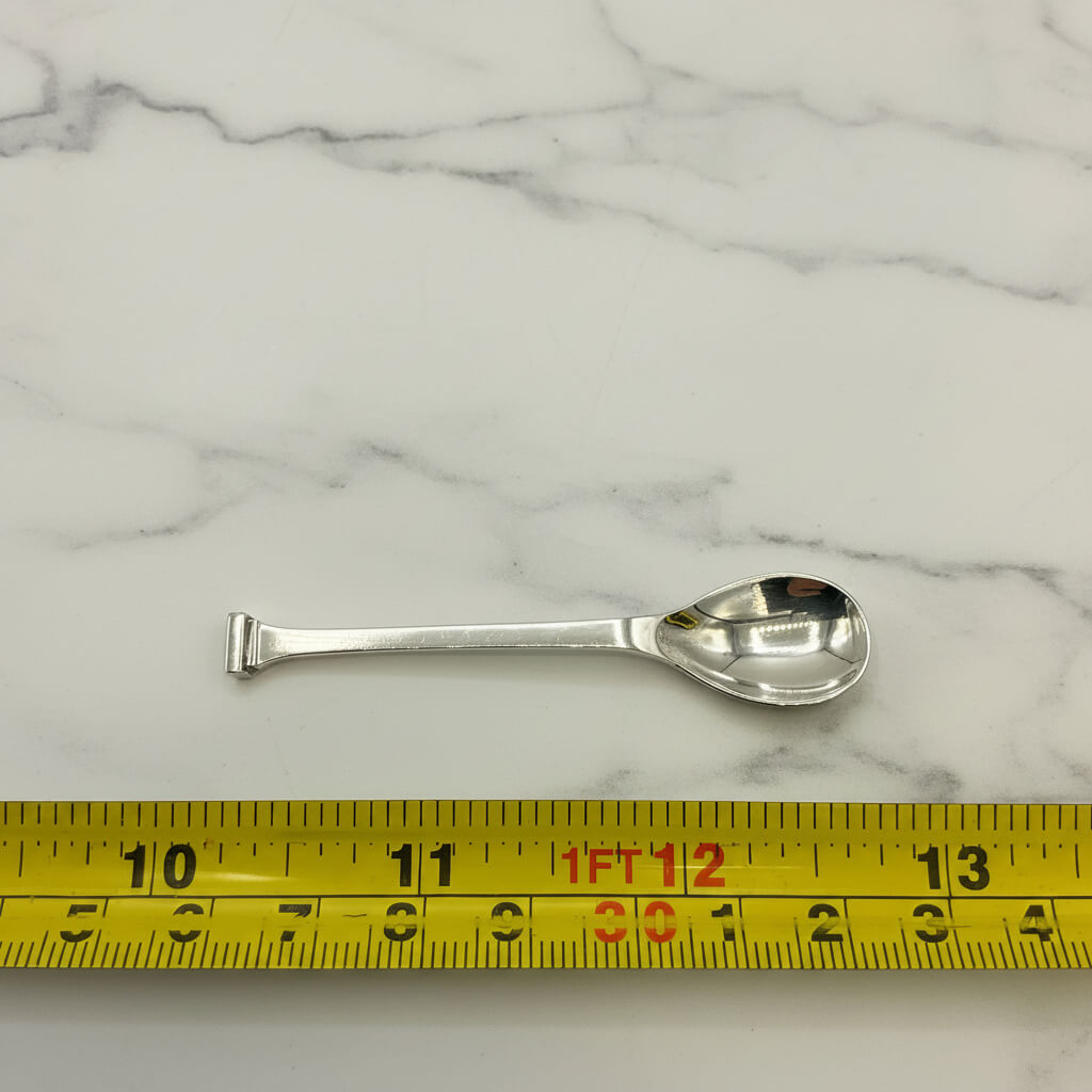 Silver salt spoon on a marble surface with a yellow measuring tape for scale.