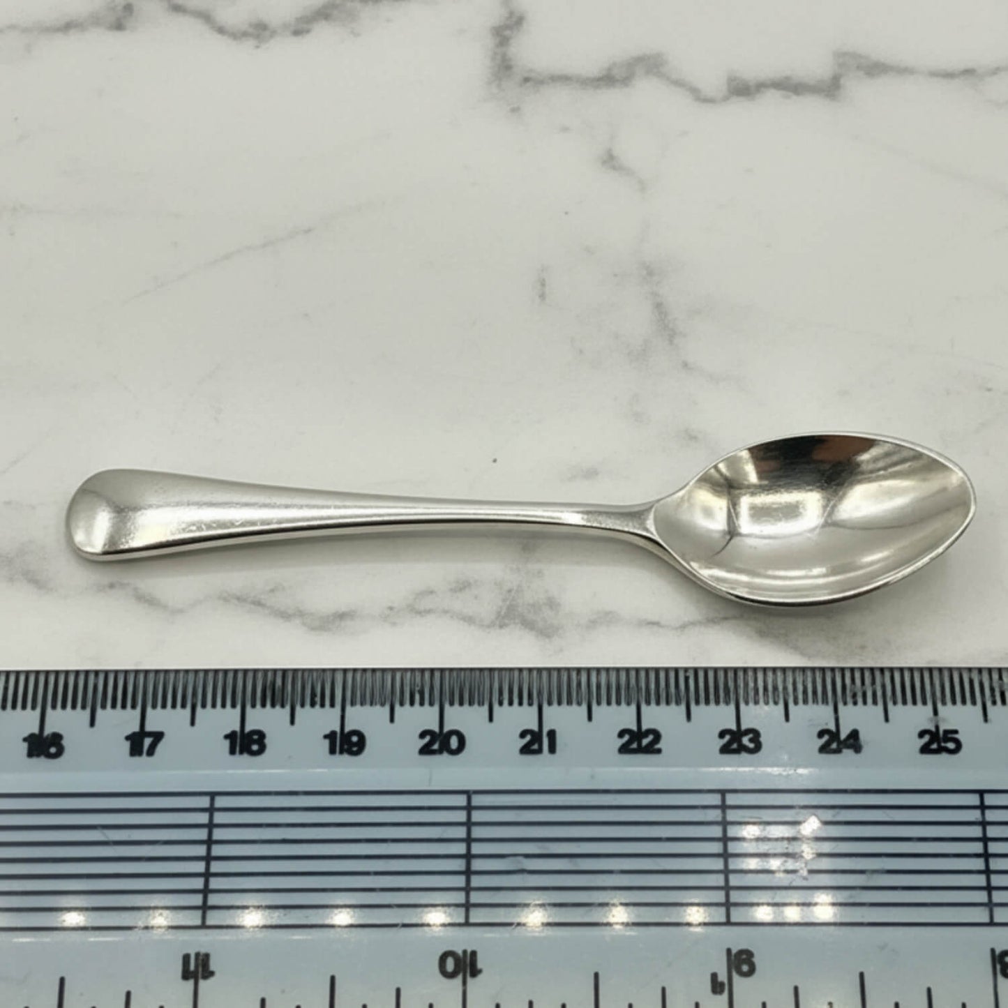 Silver coffee spoon on a marble surface with a ruler for scale
