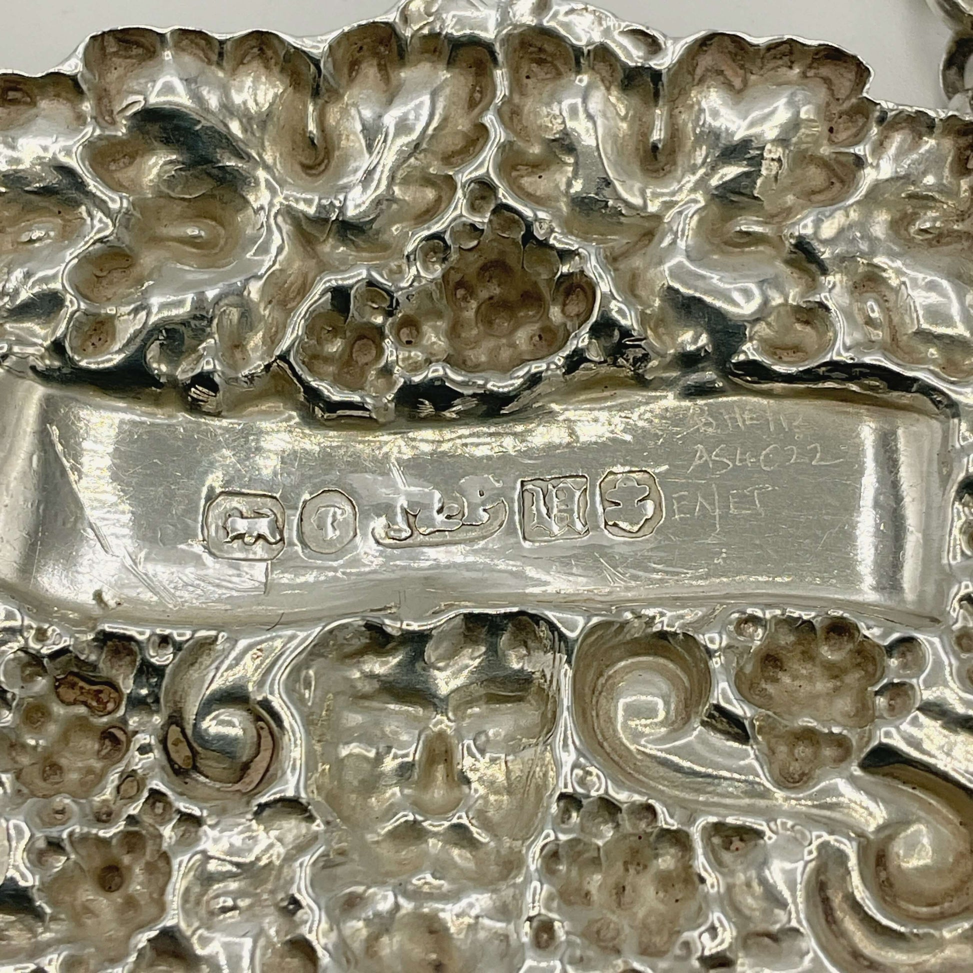 Close-up of a back of a silver decanter label with engraved patterns and visible hallmarks.