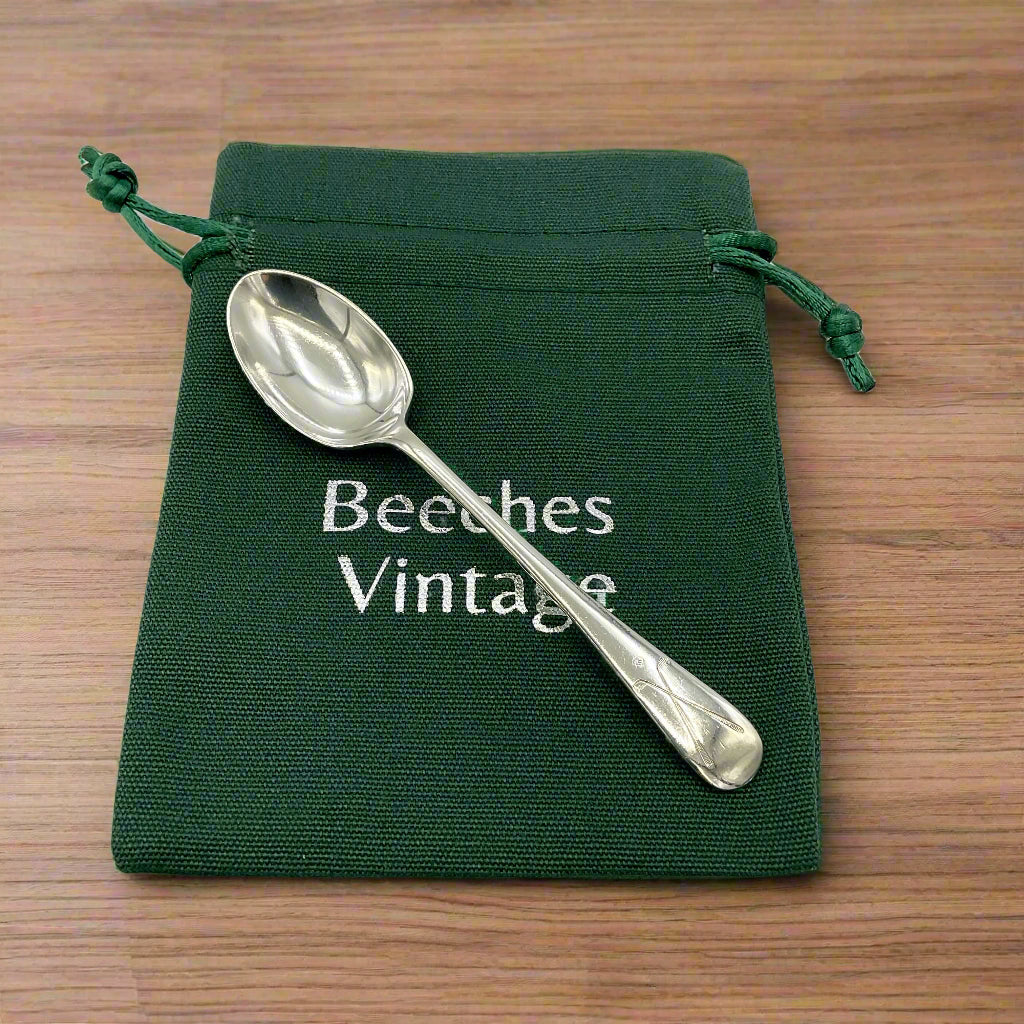 Silver spoon on a green drawstring bag with 'Beeches Vintage' text on on a wood table