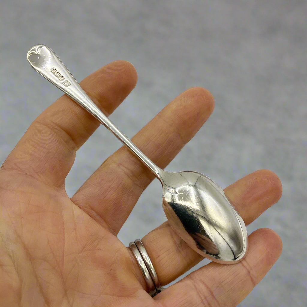 Silver spoon held in a hand against a grey background