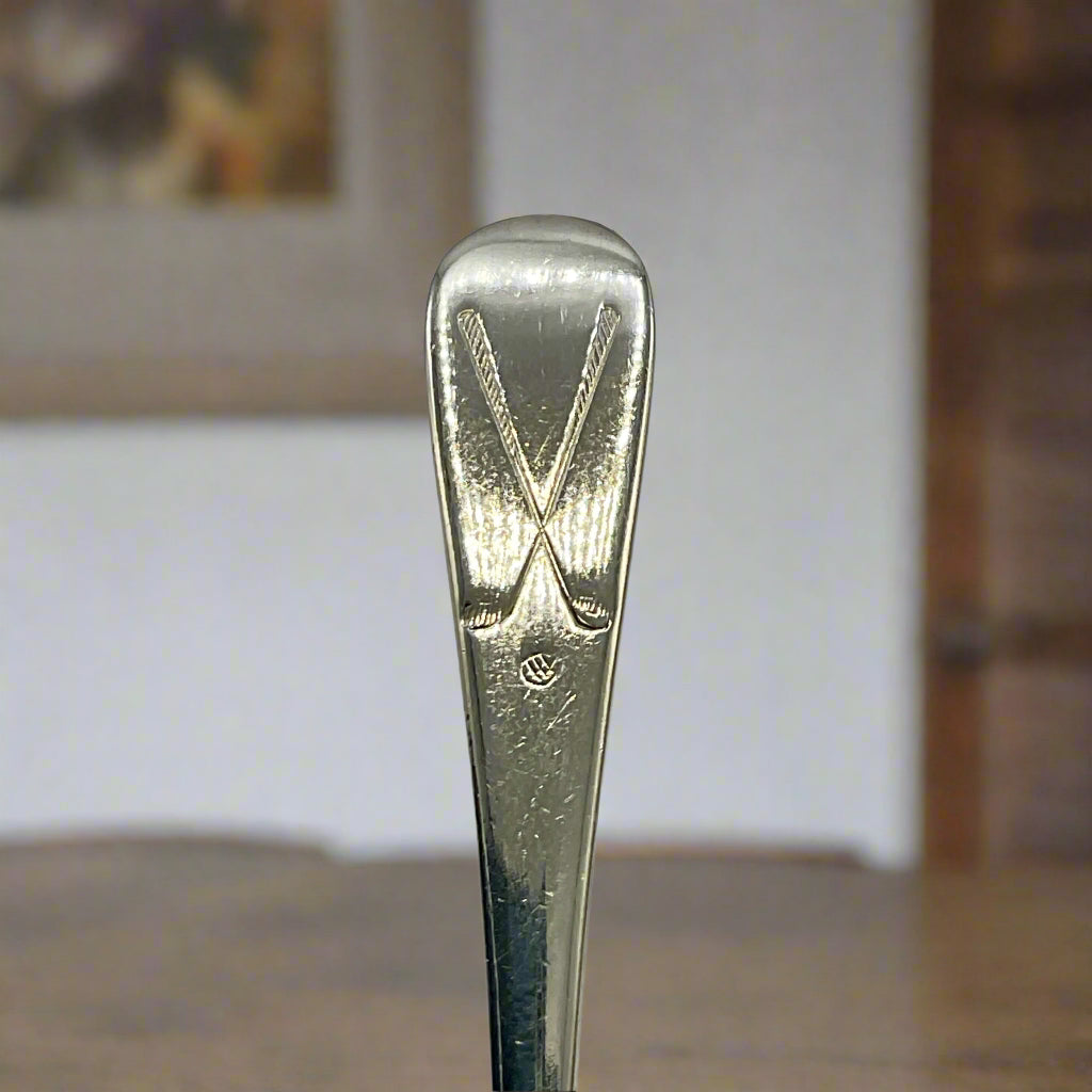 Close-up of a silver spoon handle with a golf logo with a dining room in the background
