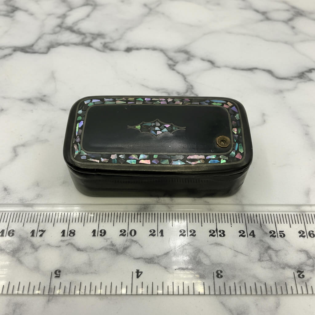 Decorative black box with mother-of-pearl inlay on a marble surface with a ruler for scale.