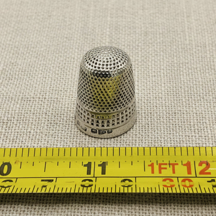 Metal thimble on a textured fabric background with a measuring tape for scale.
