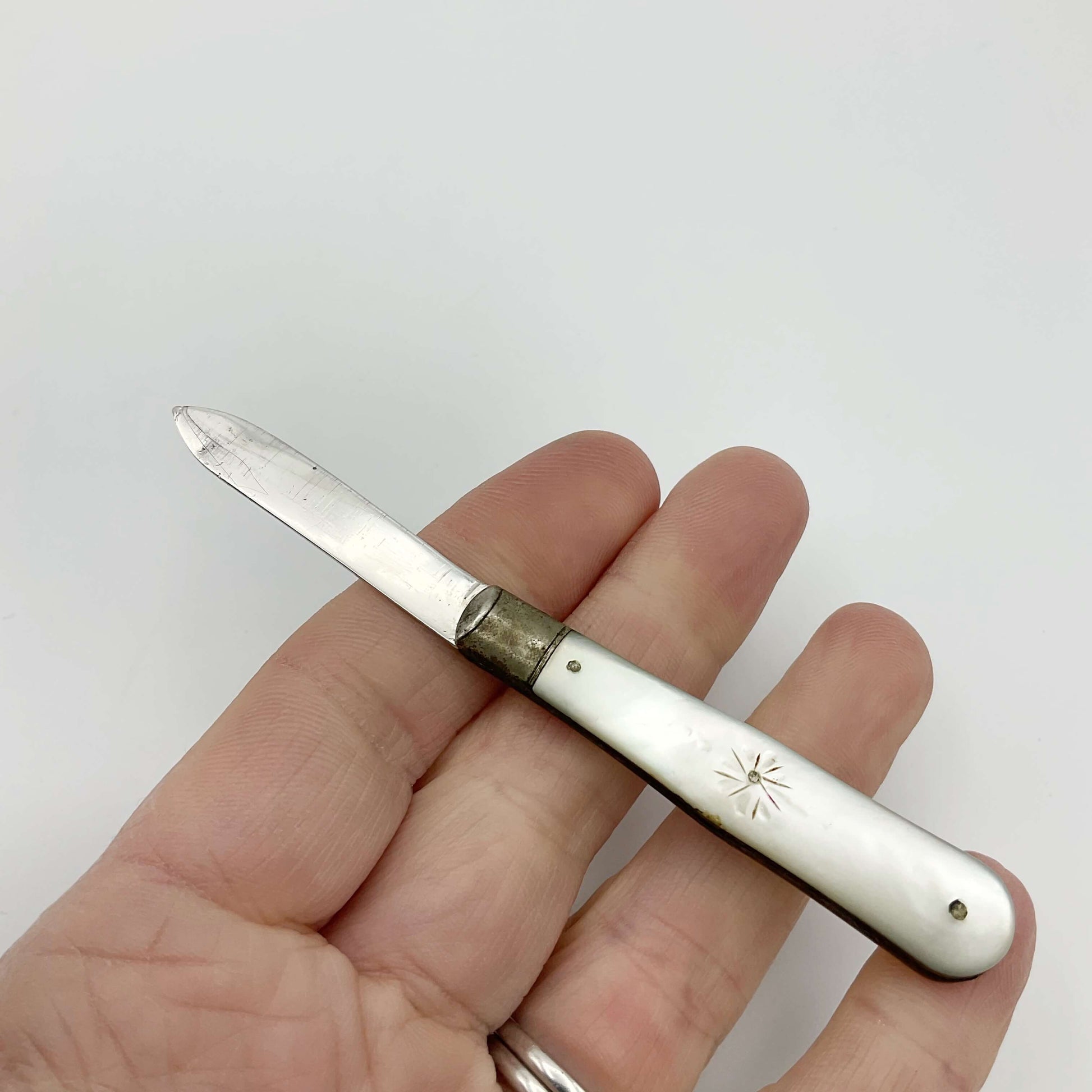 Silver fruit knife with a engraved mother of pearl handle in a hand on a white background