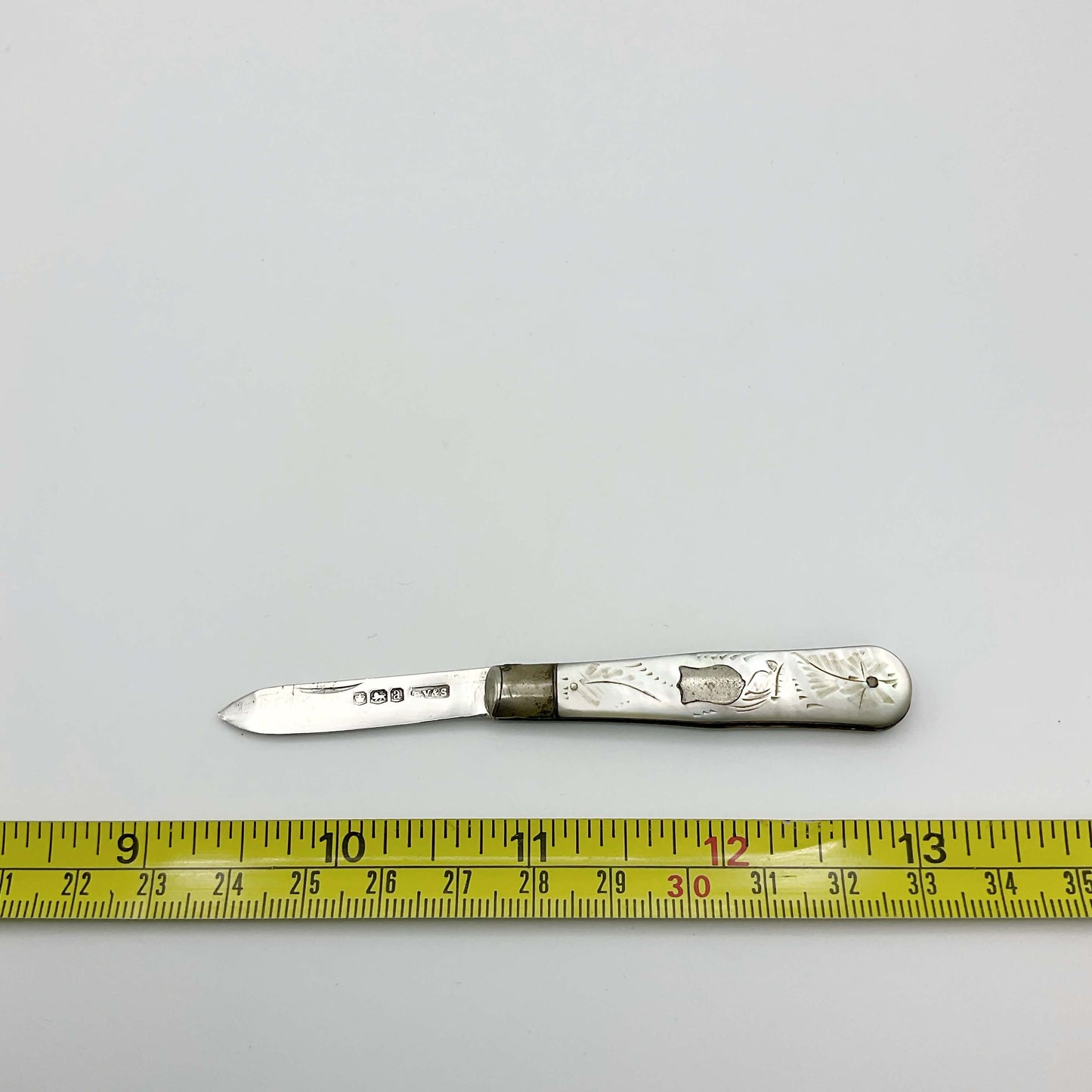 Silver fruit knife with a engraved mother of pearl handle on a white background next to a tape measure showing the length as approx 9.5cm