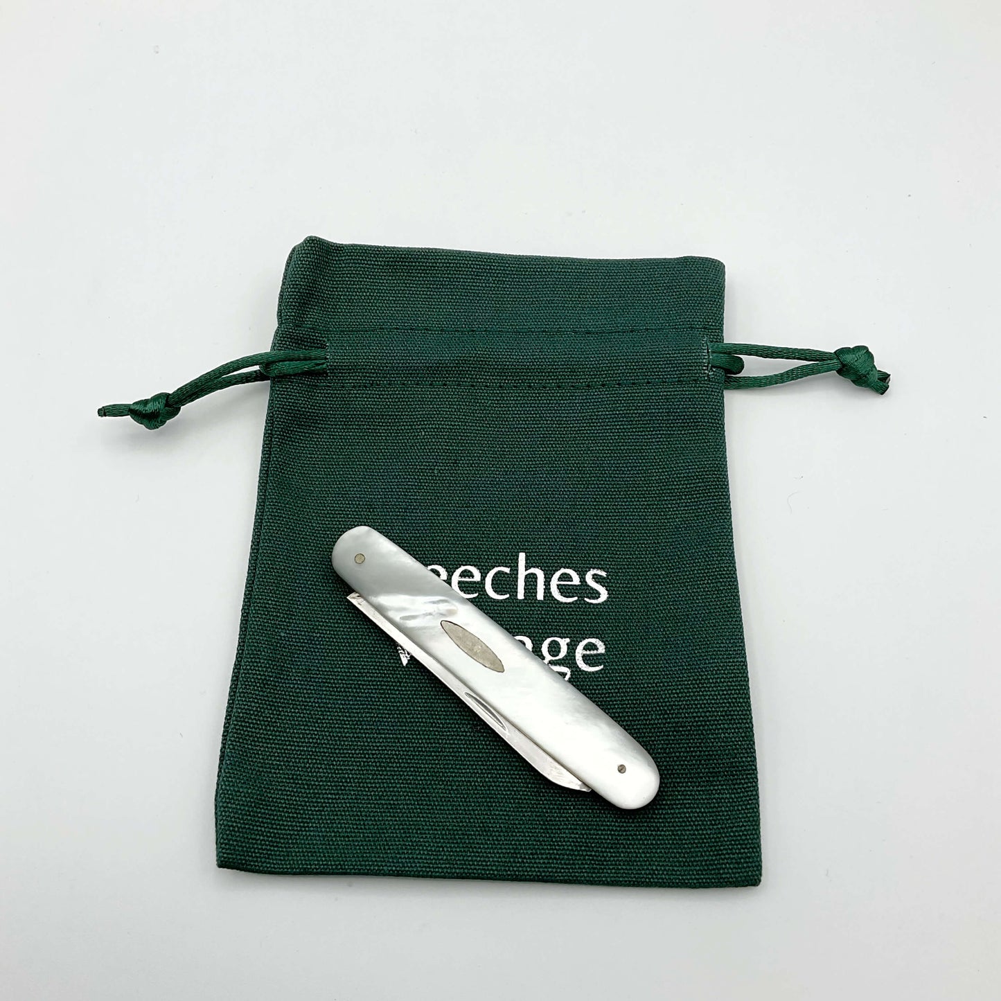 Silver fruit knife with a mother of pearl handle with blade folded away on a green gift bag and white background