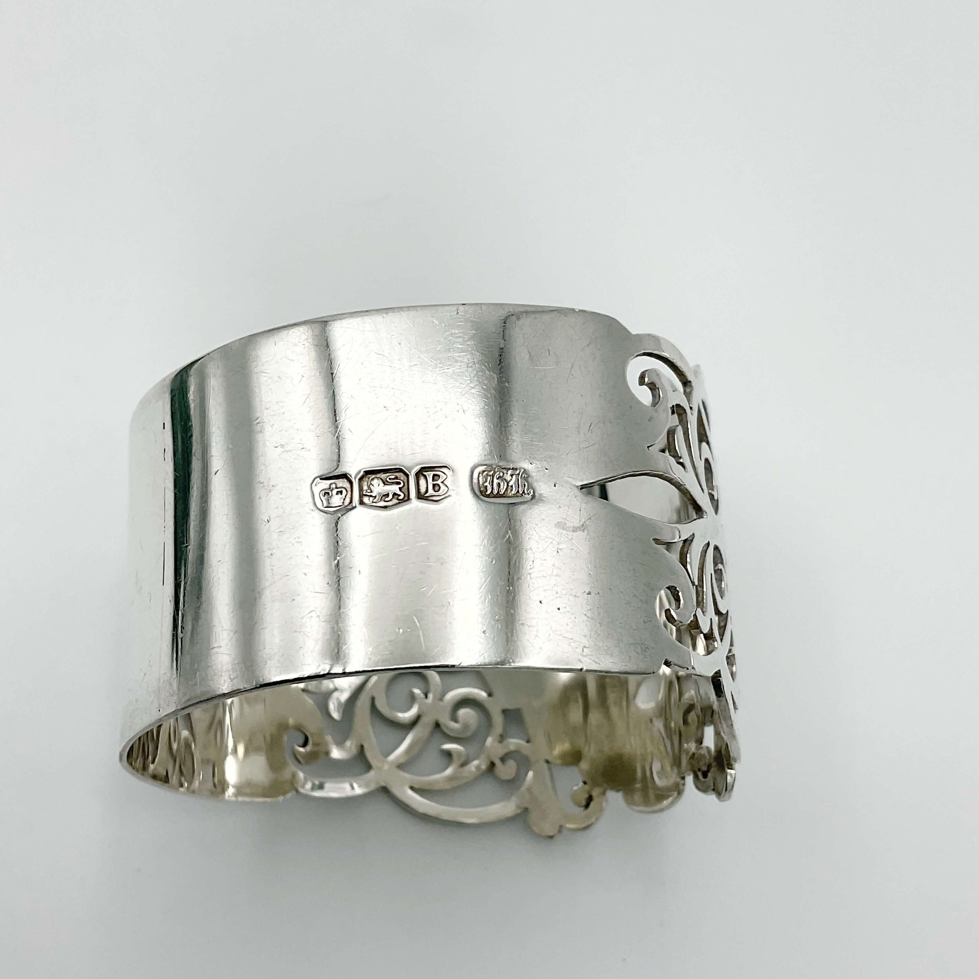Shiny napkin ring with elaborate sides and hallmarks on a plain background 