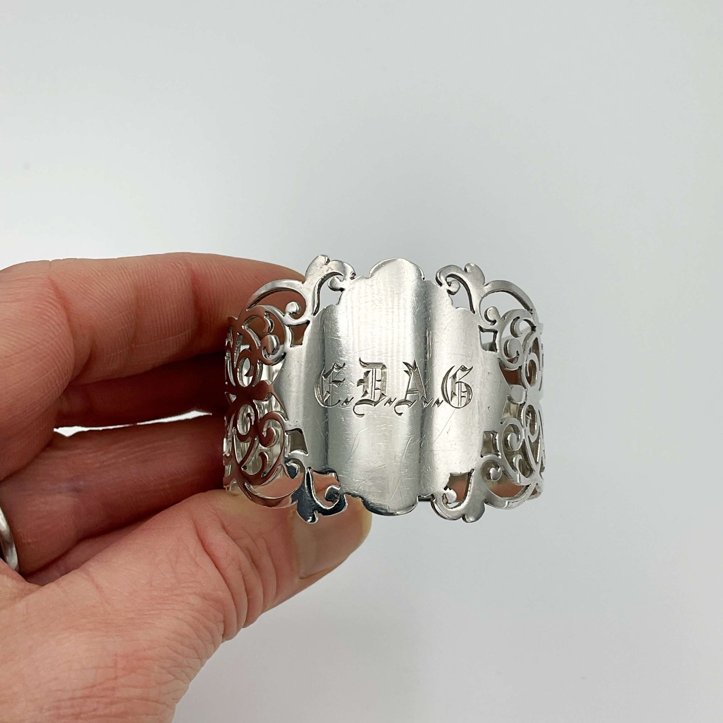 Shiny napkin ring with elaborate sides and EDAG in the centre held in a hand on a plain background 