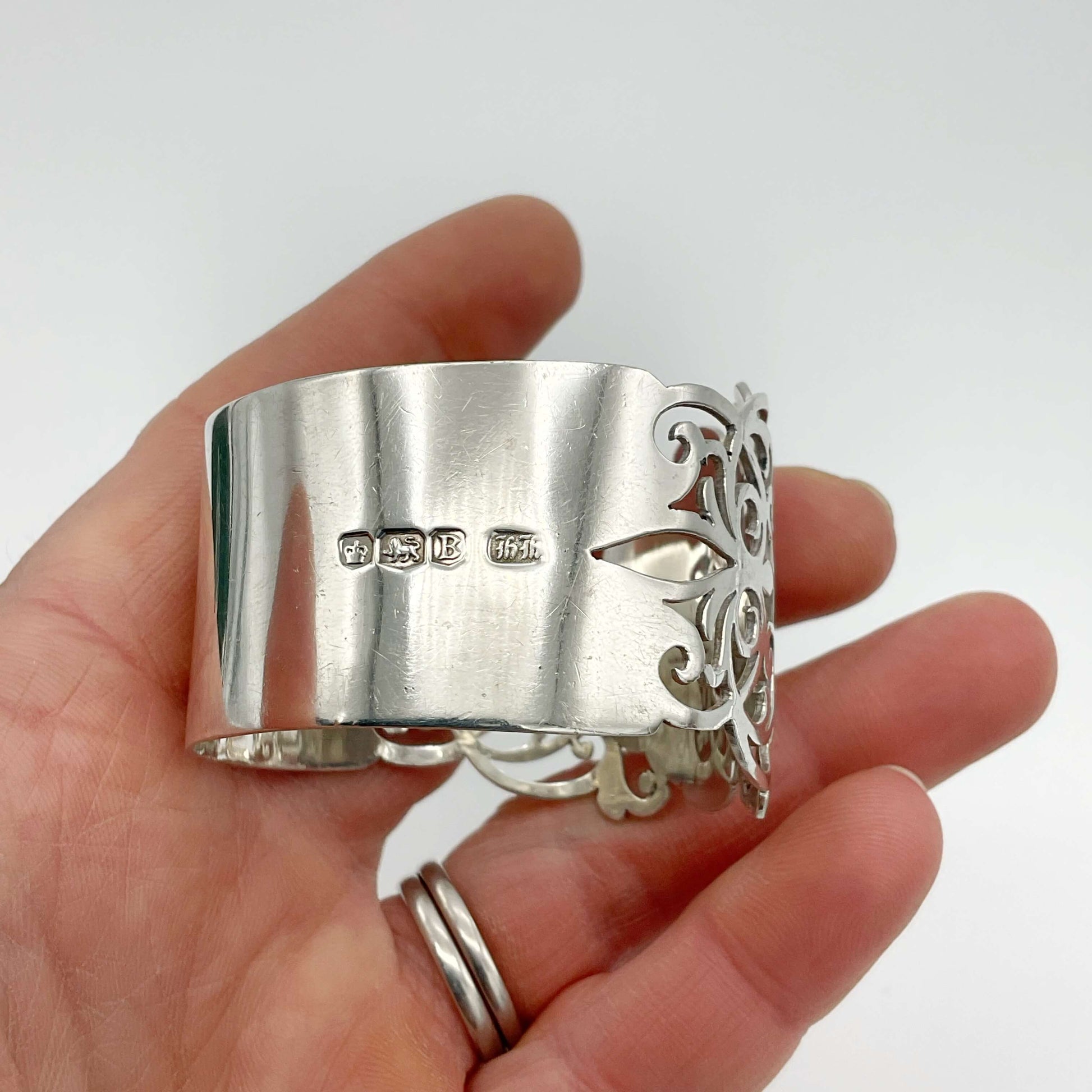Shiny napkin ring with elaborate sides and hallmarks in a hand on a plain background 