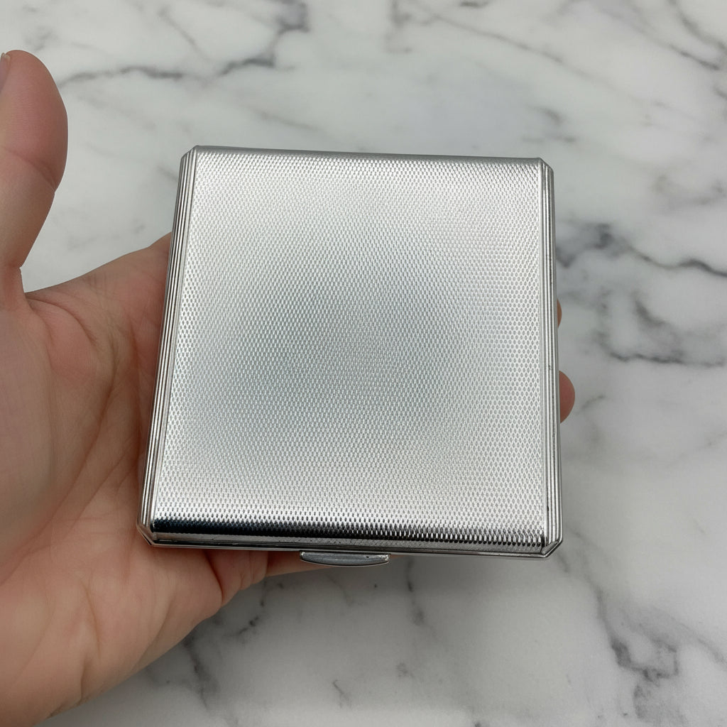 silver powder compact held in hand with a marble background