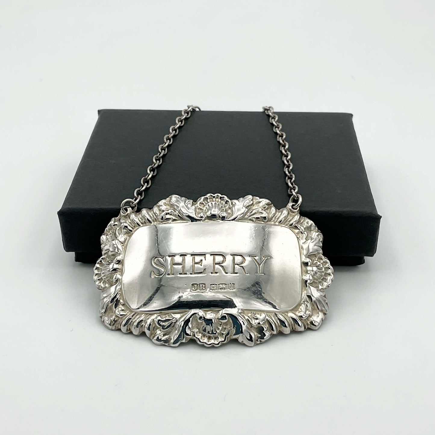 A shiny Sherry decanter label in front of a black presentation box on a white background.