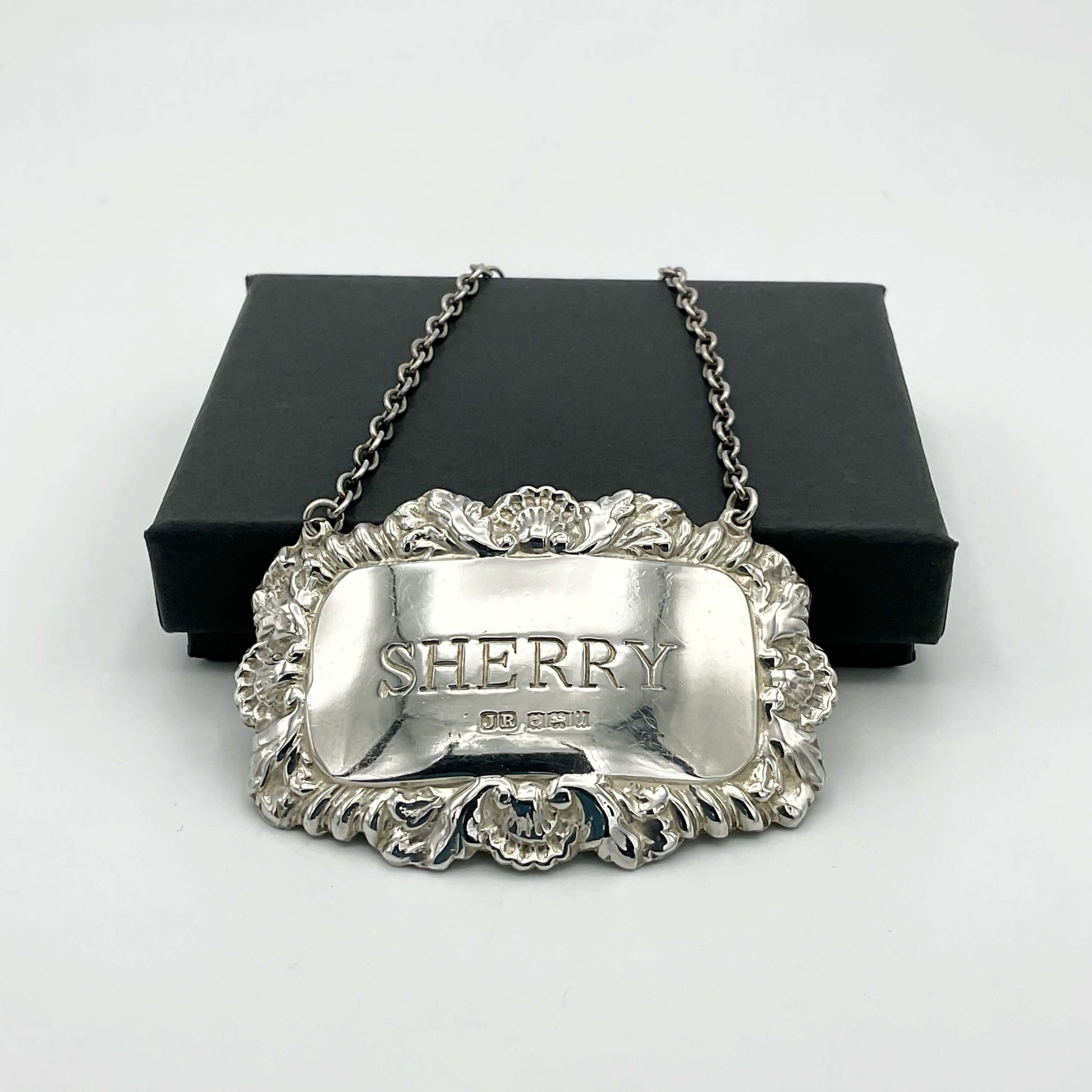 A shiny Sherry decanter label in front of a black presentation box on a white background.
