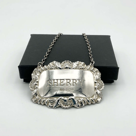 A shiny Sherry decanter label in front of a black presentation box on a white background.