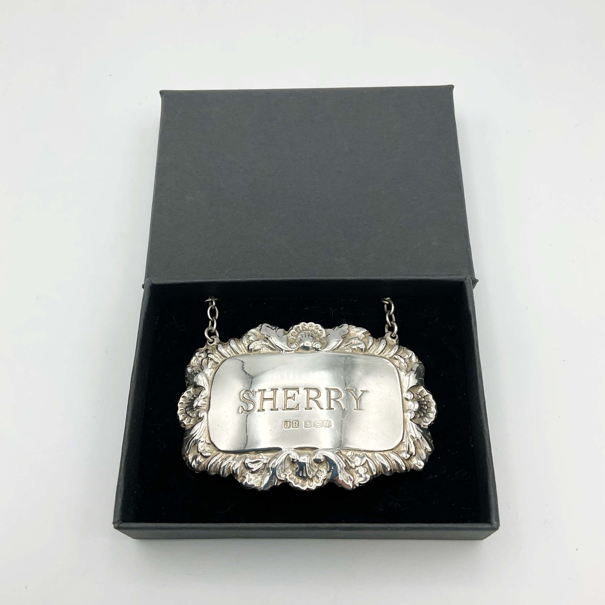 A shiny Sherry decanter label in a black presentation box on a white background.