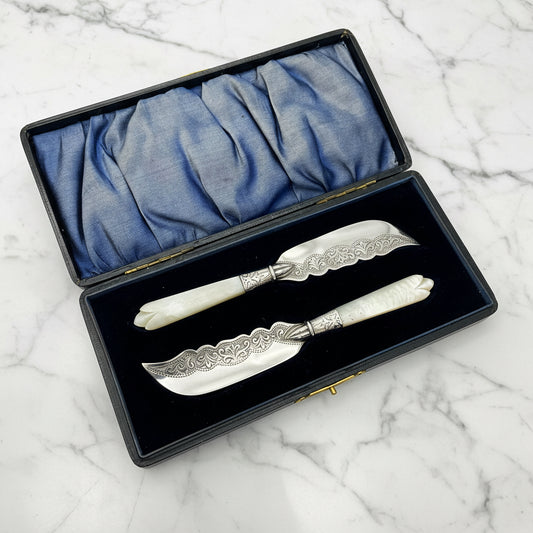 Silver butter knives in a presentation box on a marble surface