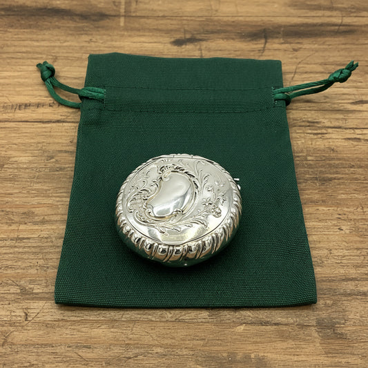 Embossed silver pill box on a green bag