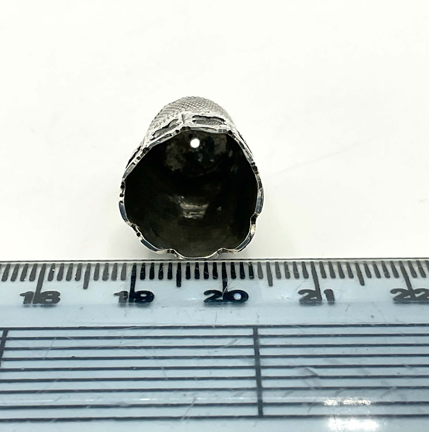 Base of Antique silver thimble next to a ruler showing the diameter measuring approximately 15mm