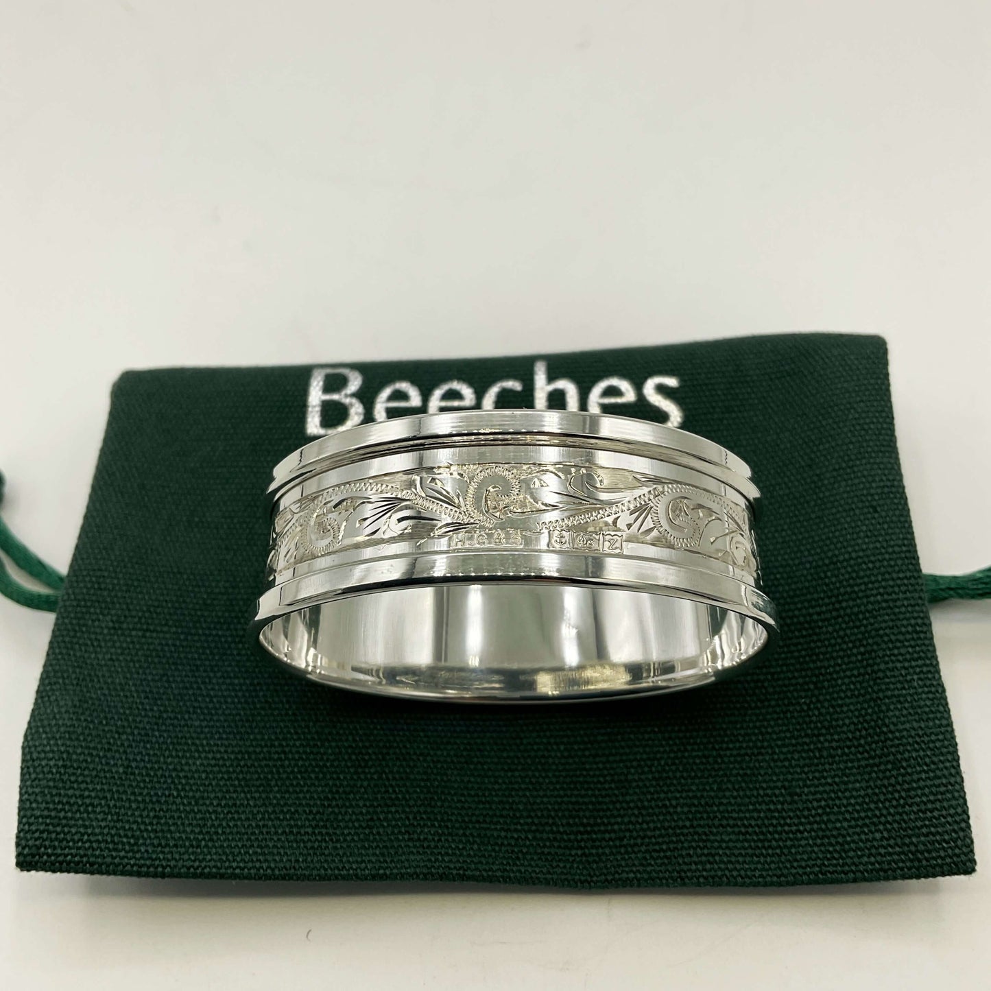 Silver napkin ring with a leaf scroll design on a green gift bag and white background