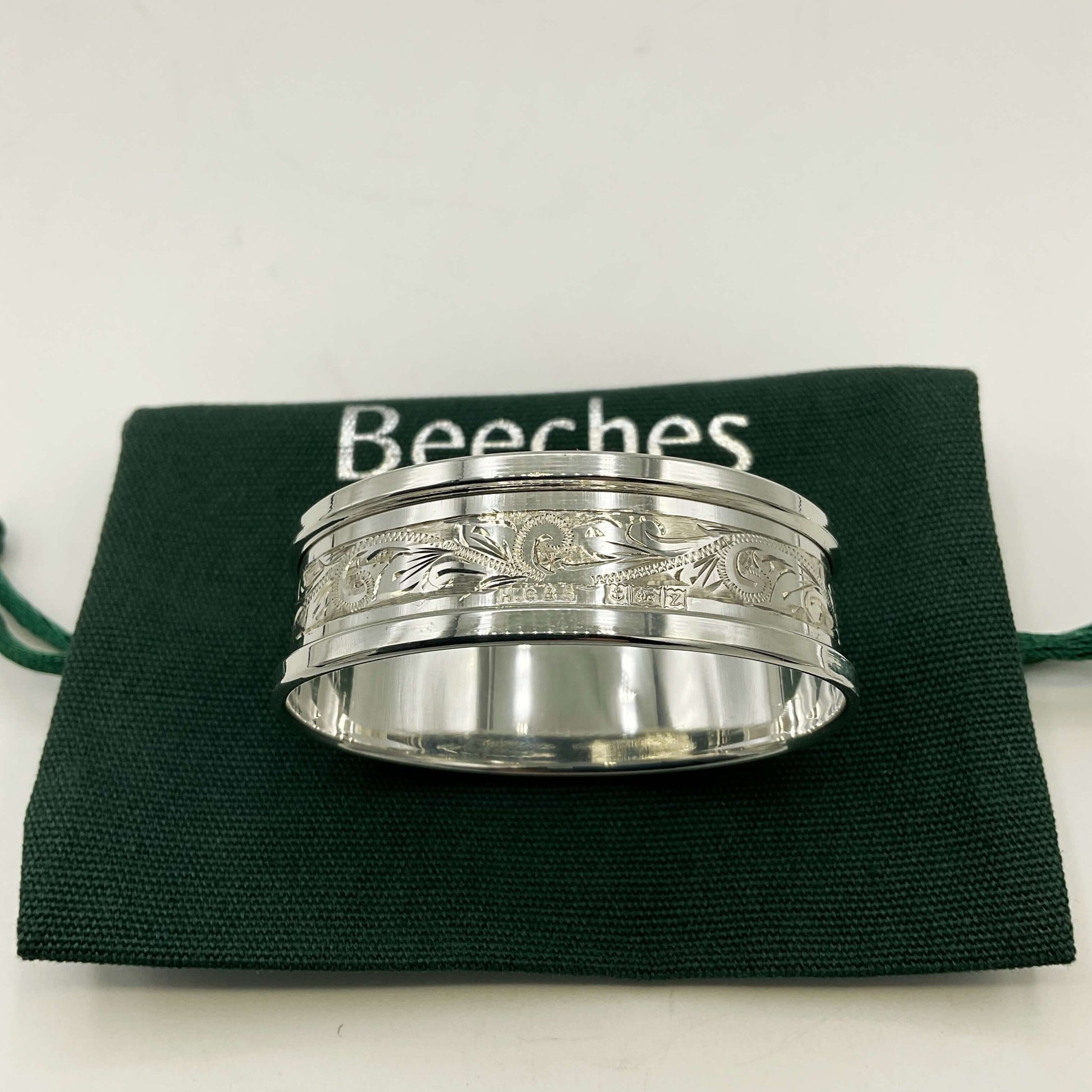 Silver napkin ring with a leaf scroll design on a green gift bag and white background