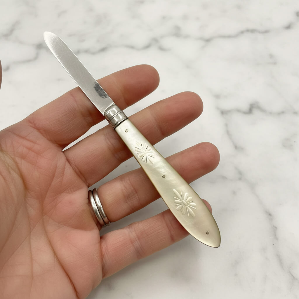 Hand holding a decorative silver knife against a marble background