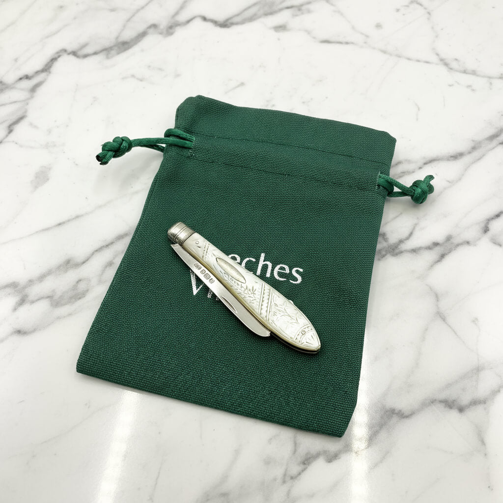 Silver fruit knife on a green drawstring pouch on a marble surface.