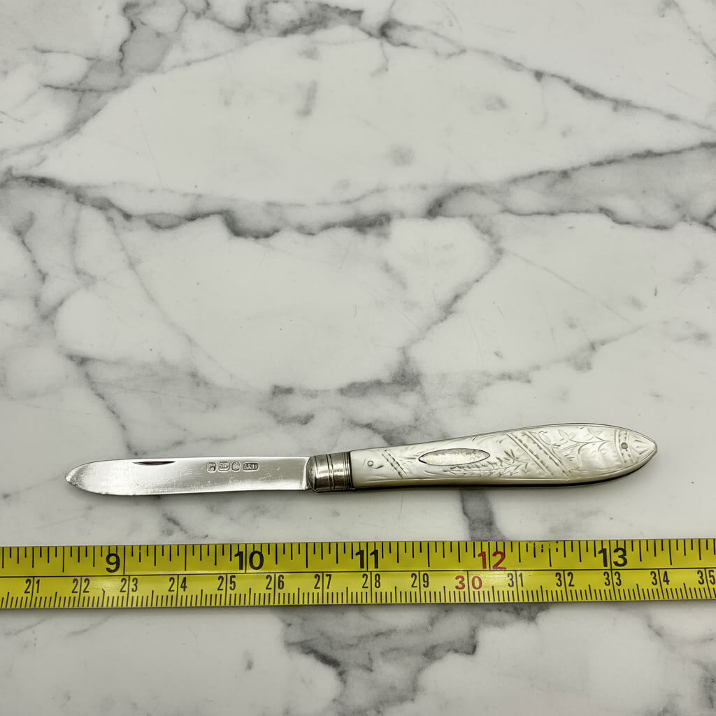 Silver knife with decorative handle on a marble surface, measured by a ruler.