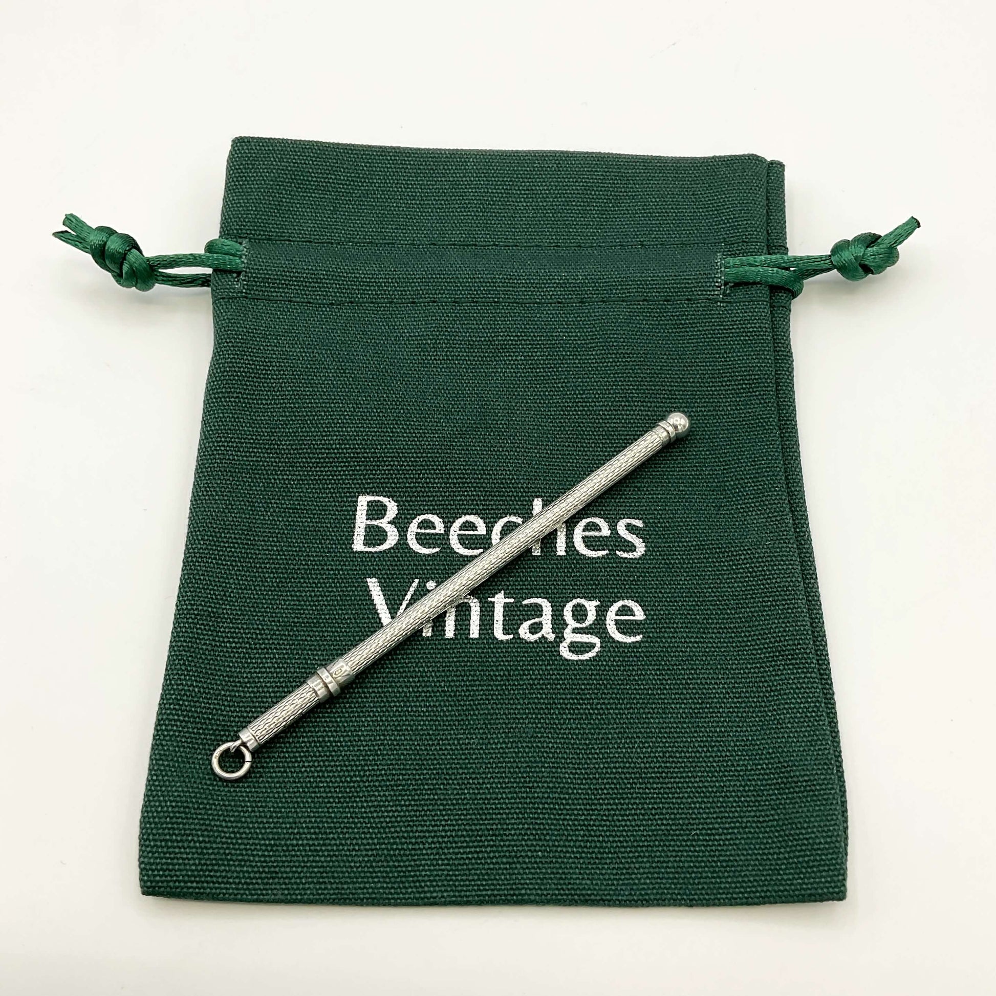 Retractable silver cocktail whisk on a green gift bag and a white background