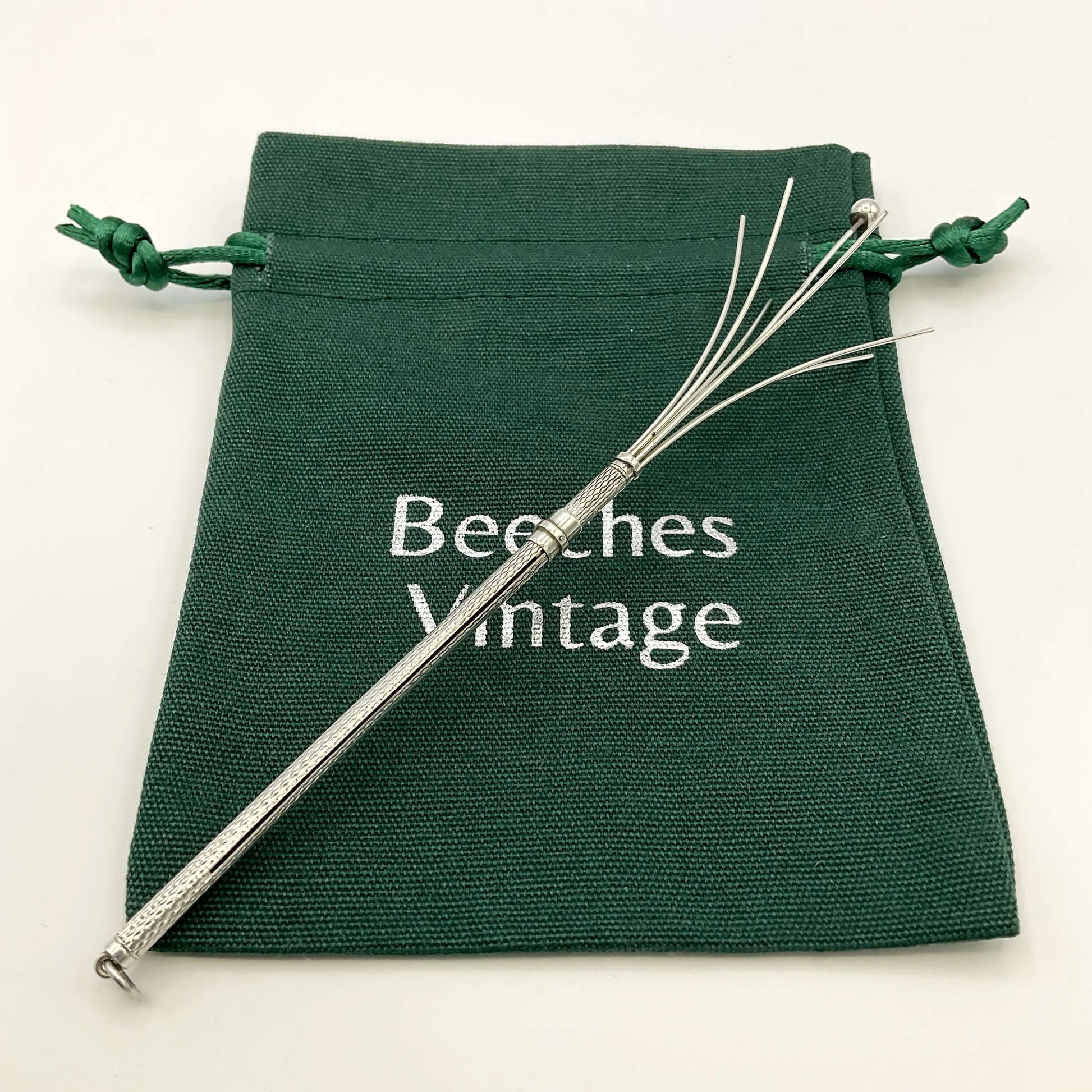 Silver whisk on a green bag with white background