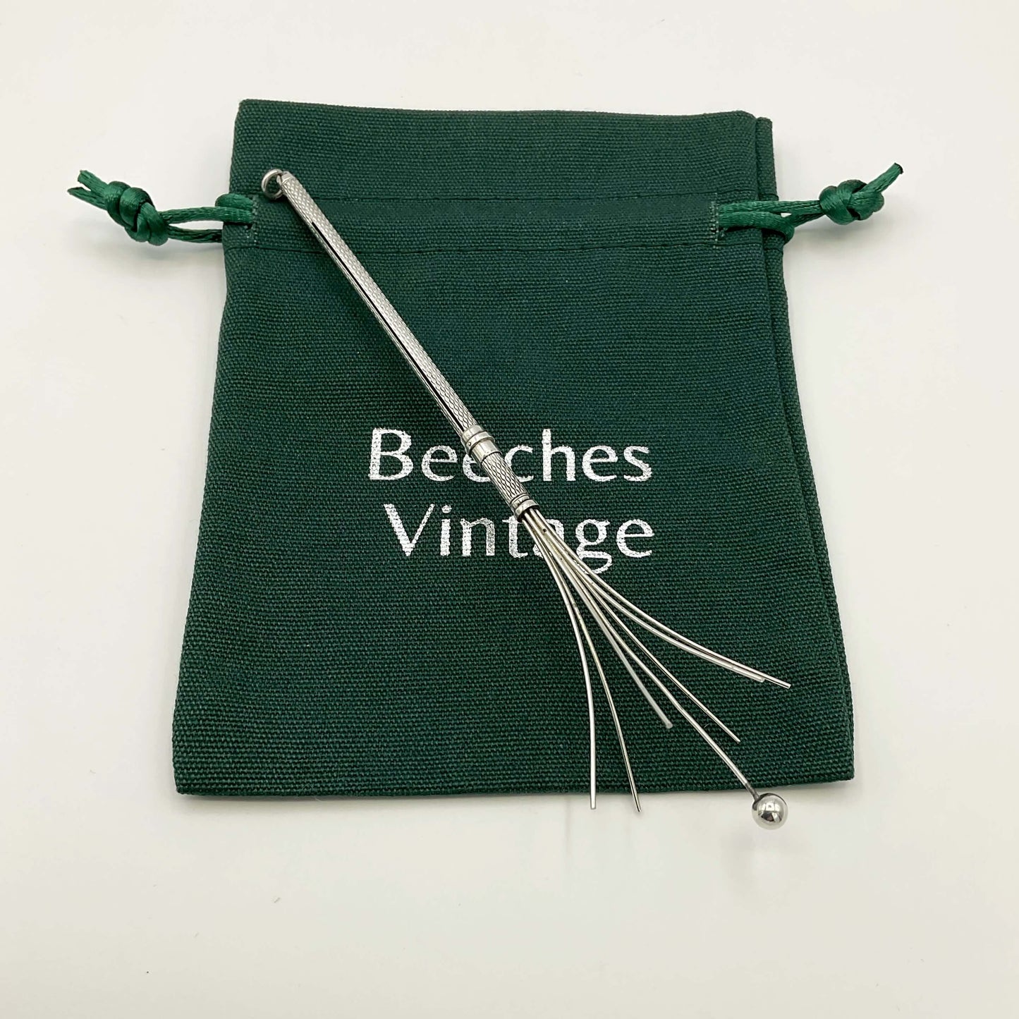 Silver whisk on a green bag with a white background