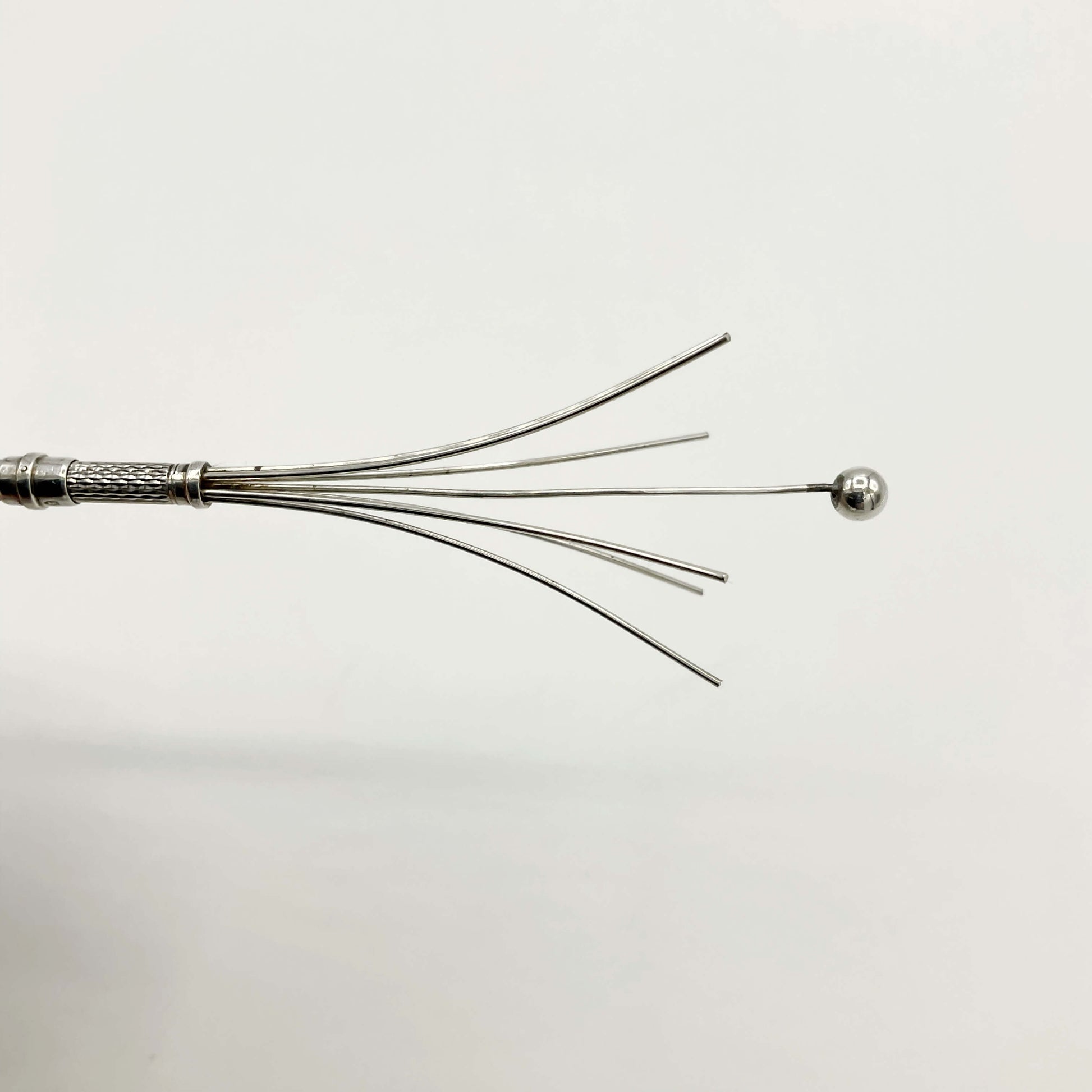 Whisk prongs of a silver cocktail whisk with a white background