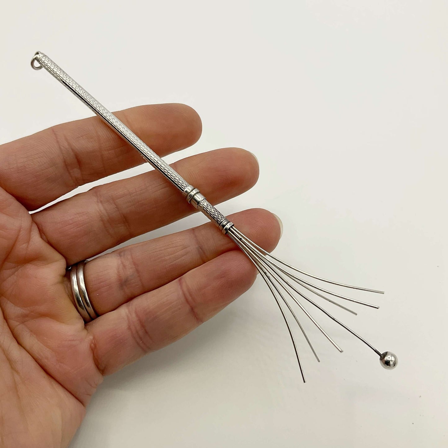 Silver cocktail whisk held in a hand with a white background
