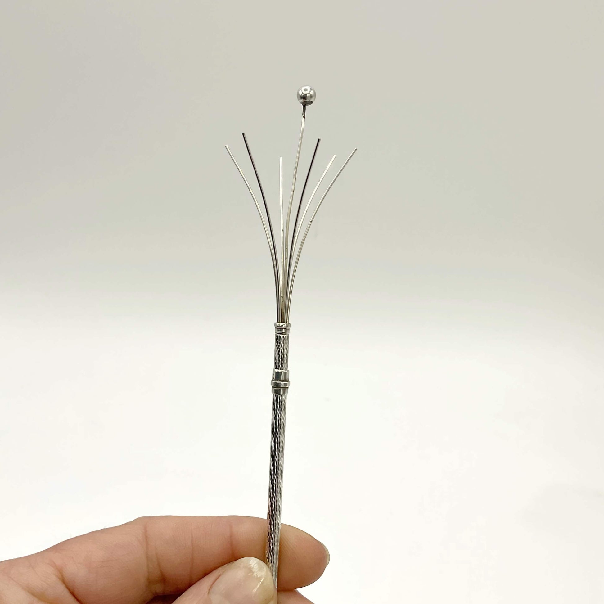 Silver cocktail whisk prongs held in a hand with a white background