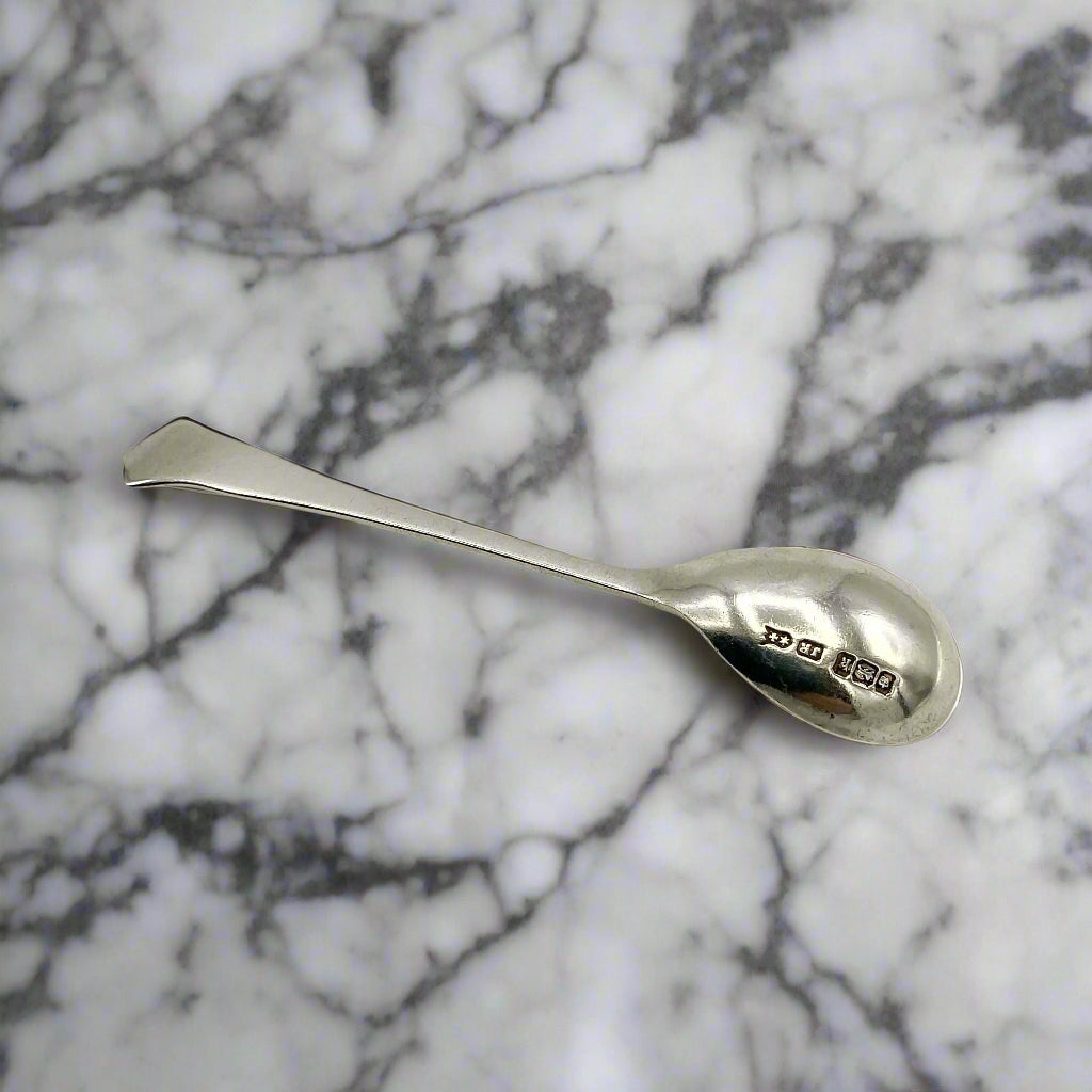 Back of a Antique Silver Art Deco Salt Spoon on a marble worktop