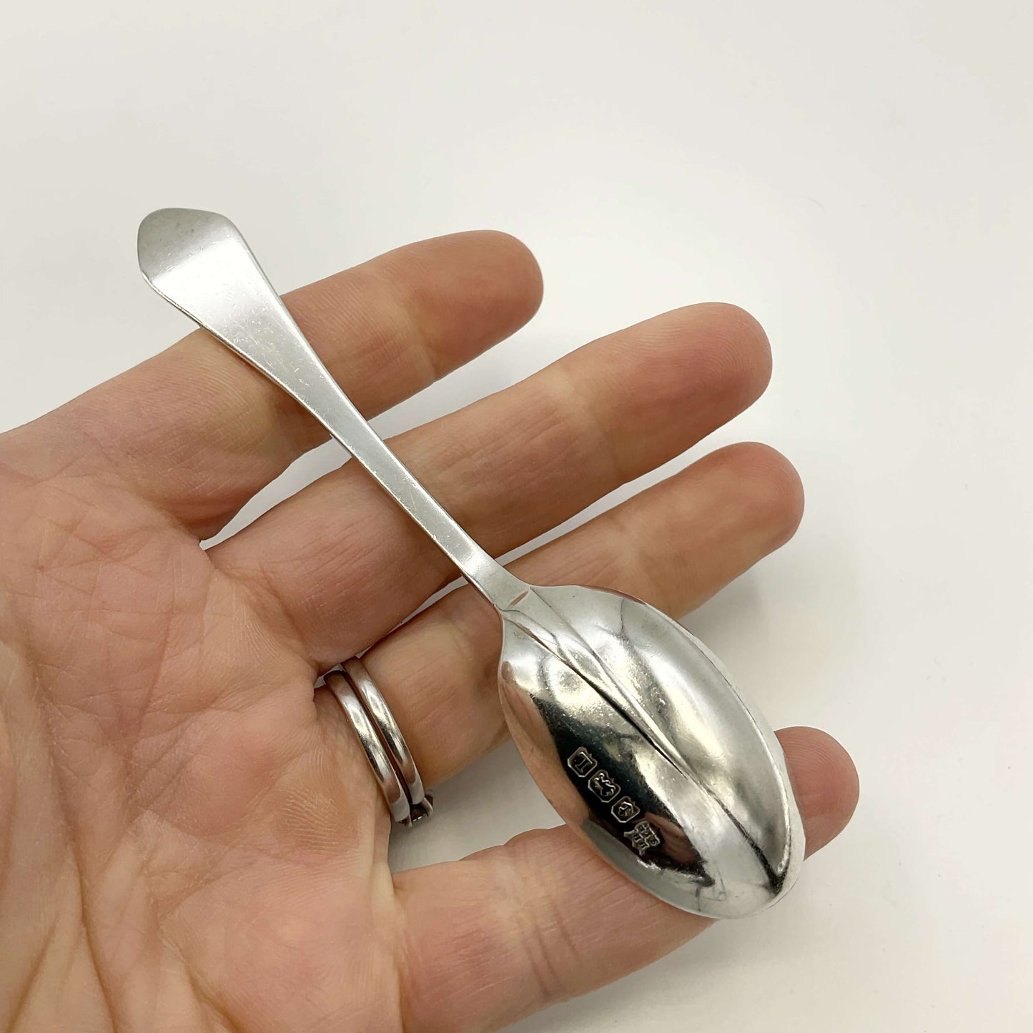 Back of silver coffee spoon held in a hand with a white background
