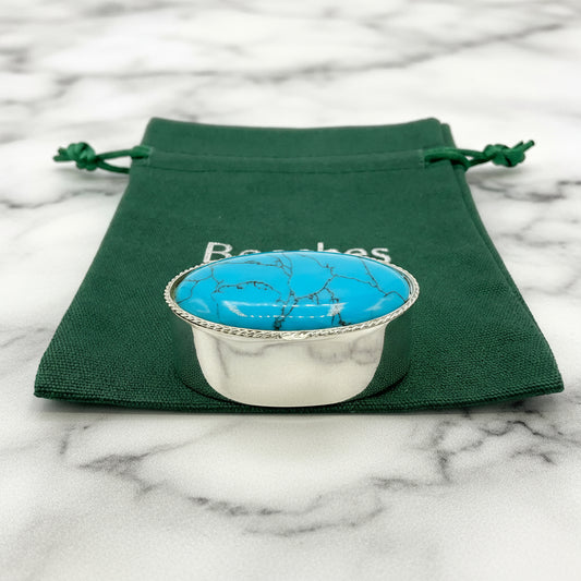 Silver turquoise pill box on a green gift bag and a marble background