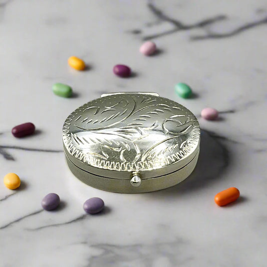 Small silver pill box surrounded by small pills on a marble worktop