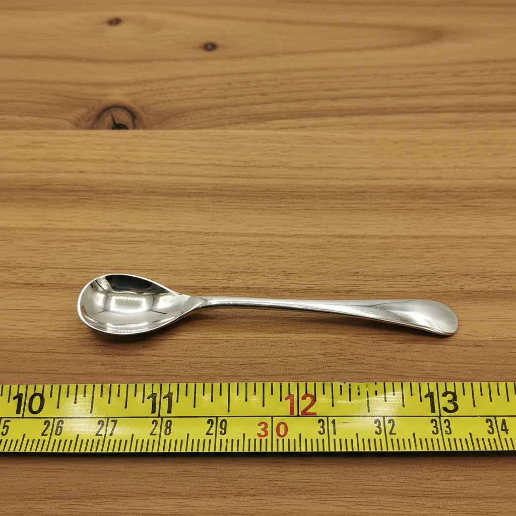 Silver salt spoon next to a tape measure showing the length as 7.7cm