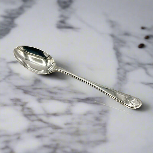 Silver coffee spoon on a marble worktop with a couple of tiny cofee beans in the background