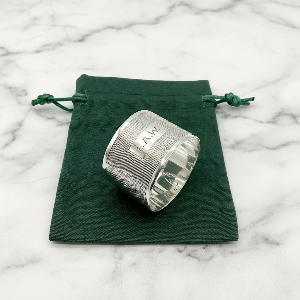 Silver napkin ring with LAW engraved on the front on a green gift bag and marble background