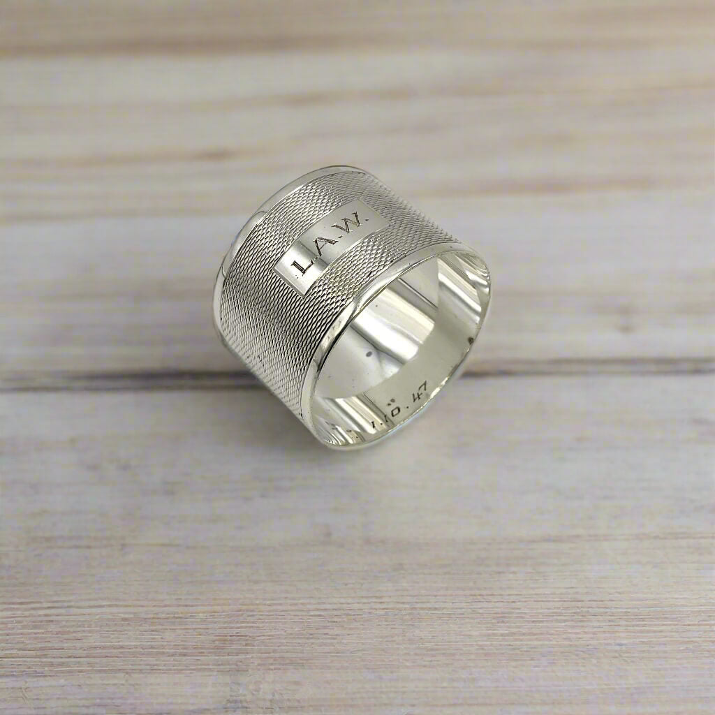 Silver napkin ring with LAW engraved on the front on a light wood table