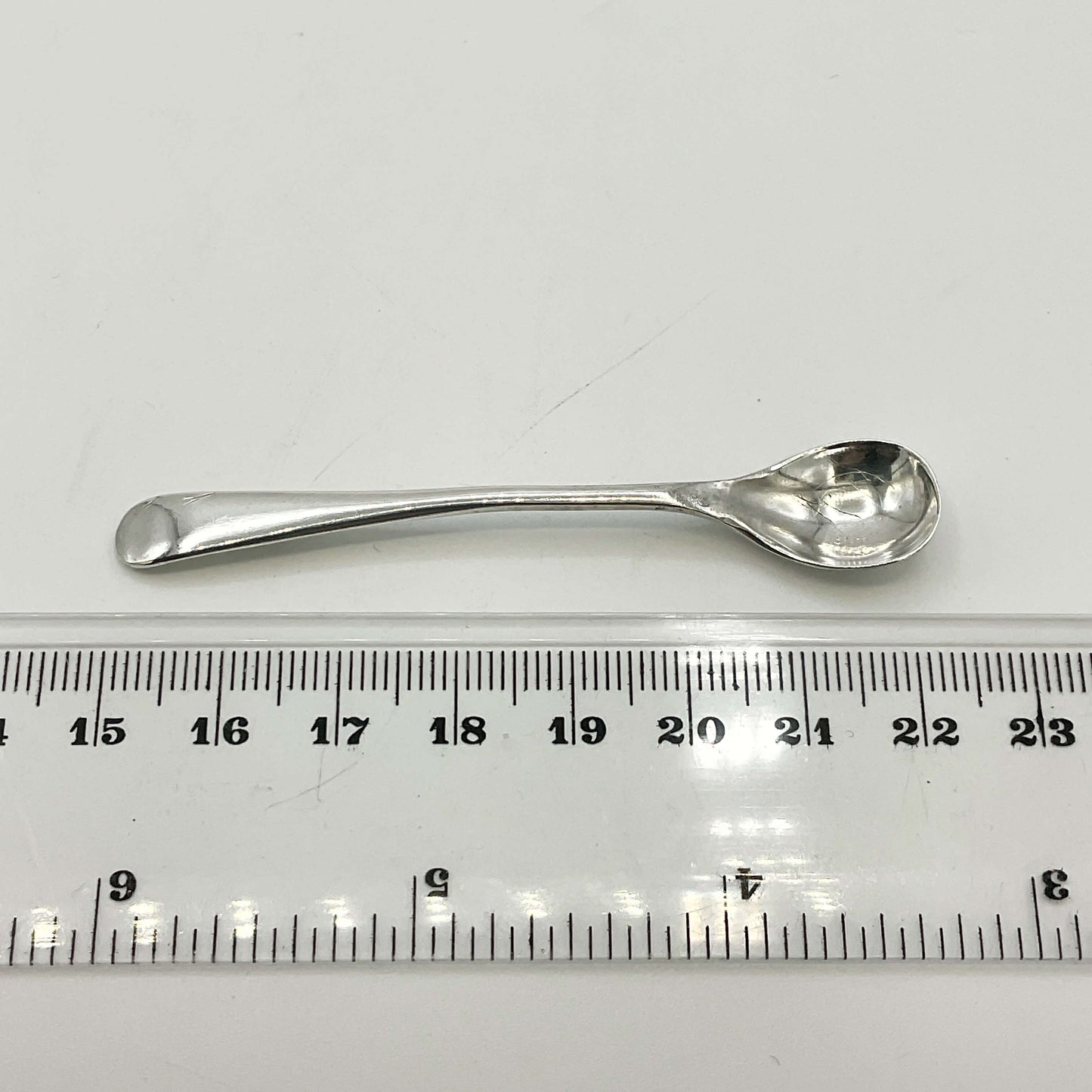Silver spoon next to a ruler on a white background