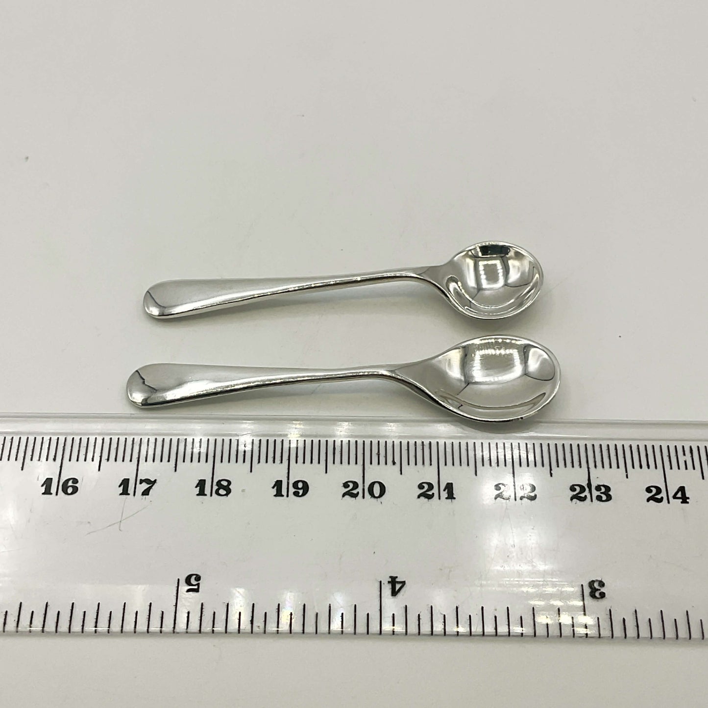 Two silver spoons next to a ruler on a white background